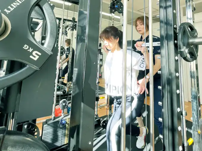 女性がトレーナーとウェイトトレーニングをしている