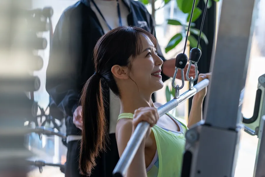 明るいジムで笑顔で筋トレに励む女性。ダイエットにおける筋量維持と基礎代謝アップの重要性を解説