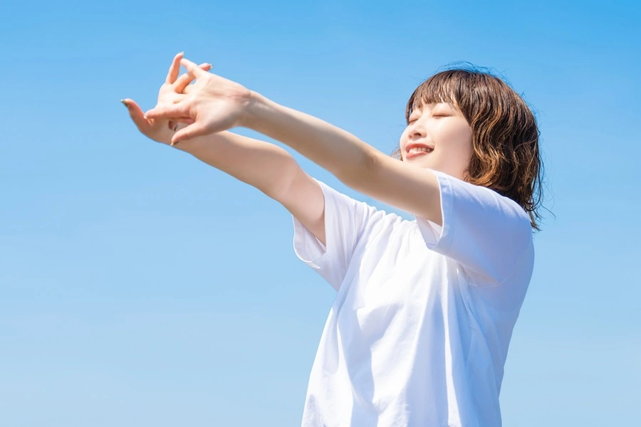 青空の下で気持ちよくストレッチをする女性。糖尿病予防に効果的な有酸素運動と習慣化のイメージ